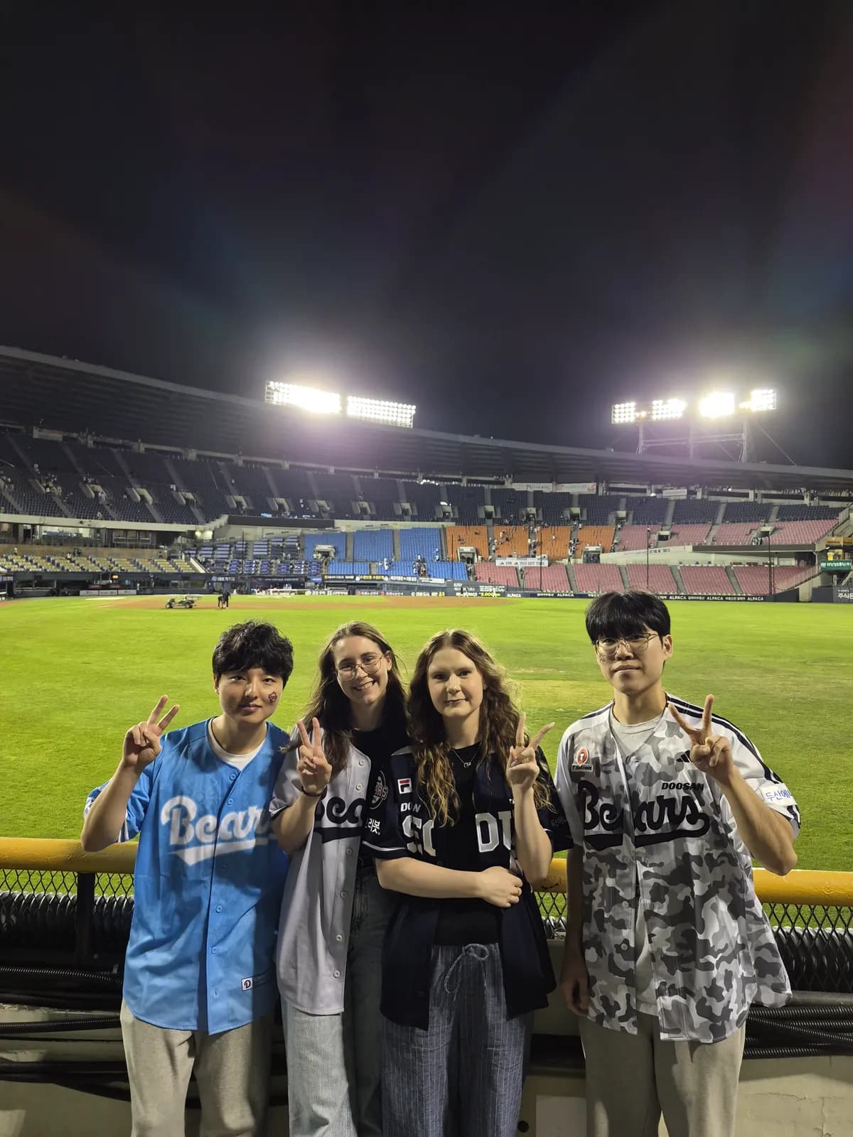 Four guests in front of the Jamsil outfield under the night lights